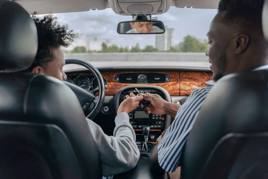 An instructor handing car keys to a student in the driver's seat