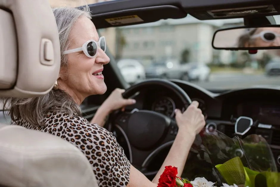 A senior driver smiling behind the wheel on a palm-lined street